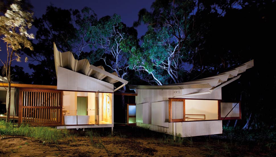 Bedroom and bathroom pods are constructed with fibrous cement sheeting, and connected by a timber bridge hovering above the ground.