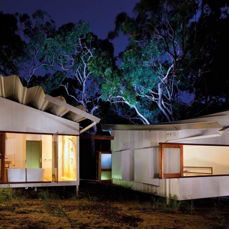 Bedroom and bathroom pods are constructed with fibrous cement sheeting, and connected by a timber bridge hovering above the ground.